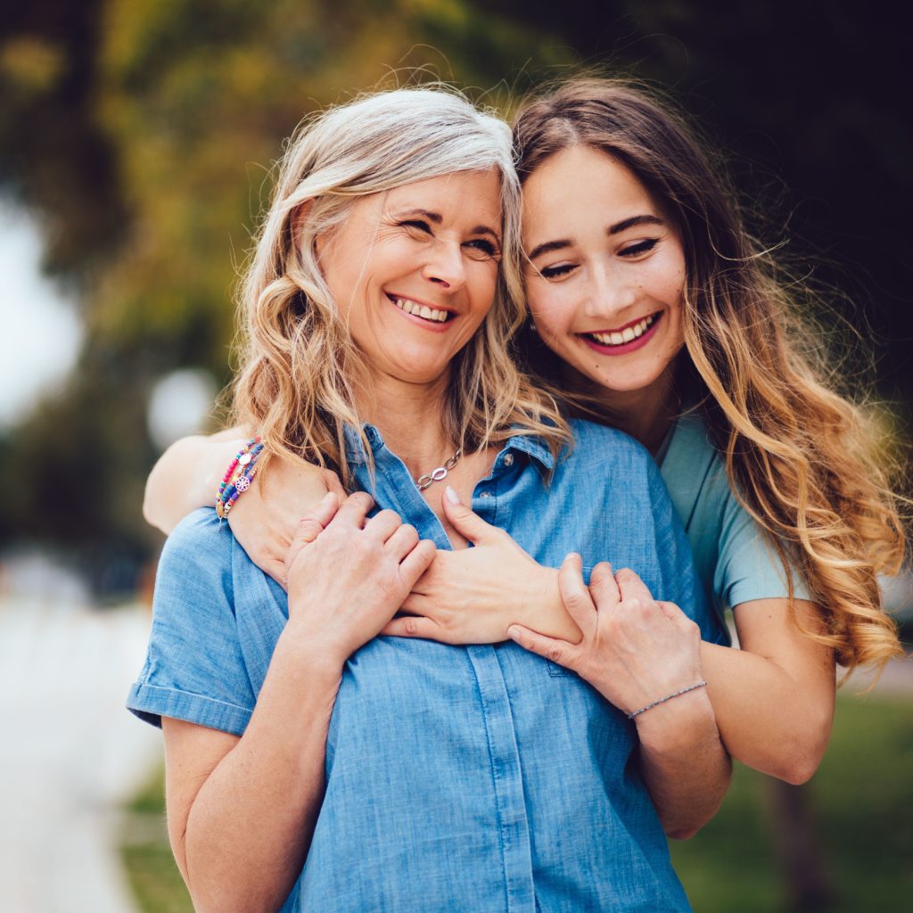 Smiling mother and daughter laughing and hugging outdoors