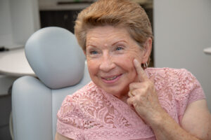 Woman at Periodontal Health Center, real patient, in exam chair, smiling pointing at smile, dental implants in New Port Richey and Tampa, FL