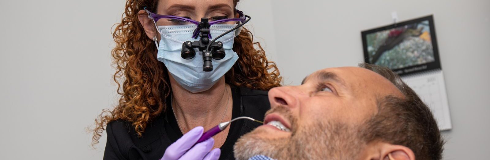 Periodontist examining patient's teeth with dental microscope and instruments.